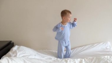 Mavi çizgili pijamalarıyla yatakta zıplayan, gülümseyen ve şarkı söyleyen tatlı çocuk. Mutlu çocukluk kavramı. 