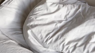 Küçük çocuk sabah erken kalkar ve battaniyenin altında parlak güneşten saklanır. Gerçek insanlarla yaşam tarzı görüntüleri..