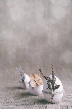 Sıfır atık, vegan, sürdürülebilir Paskalya dikey afişi. Doğal çuval bezi arka planında kurumuş çiçeklerle süslenmiş üç tahta yumurta. Huysuz çiçek, çevre dostu..