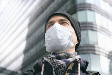 Hastalık salgını, Coronavirus covid-19 salgını, virüs koruması, kirlilik. Tıbbi koruyucu maskeli yetişkin bir adamın portresi ve arka planda ofis binası.. 
