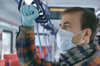 Hastalık salgını, Coronavirus covid-19 salgınını durdurmak, virüs koruması, karantina. Tıbbi koruyucu maskeli ve eldivenli yetişkin bir adam toplu taşıma araçlarında. Kendini koru..