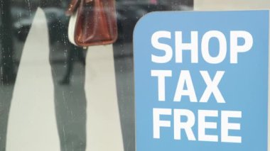 Mağazanın önündeki mağaza vergisiz çıkartma tabelası yakınlardan geçen insanları yansıtıyor. Vergisiz turist alışveriş mağazası.