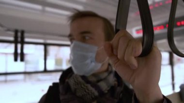 Hastalık salgını, Coronavirus covid-19 salgını, virüs koruması. Yüzünde tıbbi koruyucu maske olan ihtiyatlı bir adamın portresi toplu taşıma aracının içinde duruyor. Eline odaklan..