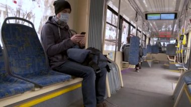 MOSCOW, RUSSIA - 16 Mart 2020: akıllı telefon kullanarak modern tramvayın içinde tıbbi maskeli yetişkin adam. Hastalık salgını, Coronavirus covid-19 salgını, virüs koruması, karantina.