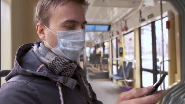 Hastalık salgını, Coronavirus covid-19 salgını, virüs koruması, karantina. Tıbbi koruyucu maskeli yetişkin bir adam akıllı telefon kullanarak boş bir toplu taşıma tramvayında..