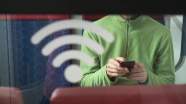 Çağdaş trende sandalyede oturan ve akıllı telefonları karıştıran bir adamın Wi-Fi sinyaliyle şeffaf duvardan bak..