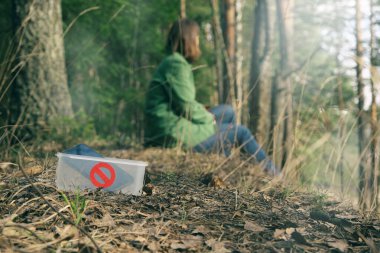 Dijital detoks konsepti. Akıllı telefonu olmayan yüzü olmayan genç bir kadın doğada dinleniyor. Parkta ya da ormanda oturan yalnız bir kız. Önünde yasaklama işareti olan bir alet kutusunda. Kopyalama alanı olan pankart.
