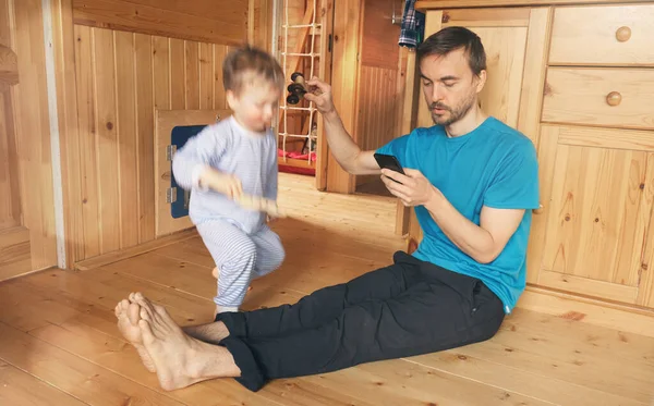 Multitasking father work from home and play with kid. Lifestyle photo of dad trying work on smartphone and his child distracts him.