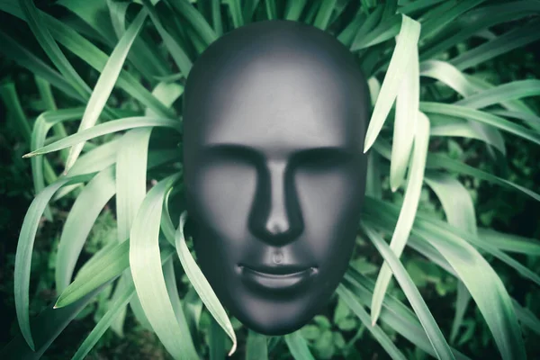 Symbiotic relationship between organic and inorganic life, artificial intelligence and nature, futuristic cyborg concept. Depersonalized human robot android face head on green plant leaves background.