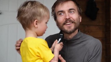 Küçük çocuk babasının sakalını kırpıcı ile kesti. Karantina süresince evde aile tıraşı, hijyen, güzellik ve kişisel bakım, yaşam tarzı konsepti.