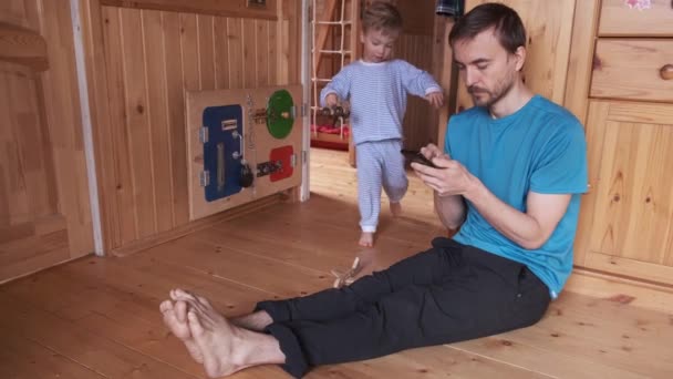 父亲在家里和孩子一起工作 爸爸试图用智能手机 他的孩子来干扰他 吸引他的注意力 玩他的身体 — 图库视频影像