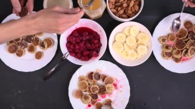 En iyi aile kahvaltısı yapıyor. Minik krep gevreği, tatlı soslar, fındık, bal ve taze ahududu. Ebeveynler ve çocuklar modaya uygun karantina yemekleri yerler. Üzerinde yemek olan bir masa..
