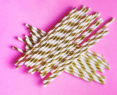 Top view of colorful paper disposable eco-friendly straws. Drinking straws with gold strips for party on pink background with copy space. Eco waste concept