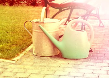 Plastik ve teneke sulama kutuları yaz bahçesindeki bir bankın yanında. Güneşli sabah ışıkları