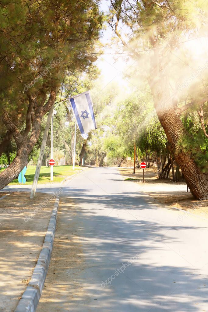 Road in Ashkelon National park. Israeli flag hanging on a tree and rays of light