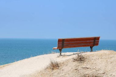 Akdeniz, Ashkelon, İsrail 'de güzel manzaralı, kırmızı, yapayalnız bir bank. Alçak tuş süzgeci