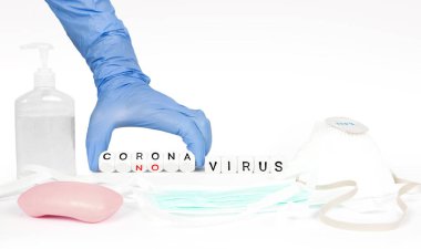 Beyaz küp bloklar ve Coronavirus kavramına sahip koruyucu aletler bir insan eliyle takla atıyor..