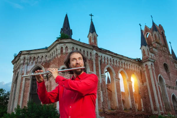 Musician in red playing the flute near an old castle at sunset — Stock Photo, Image