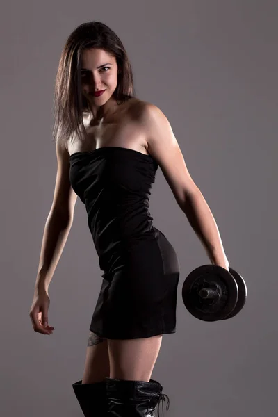 Girl in sexy black dress lifting weights — Stock Photo, Image