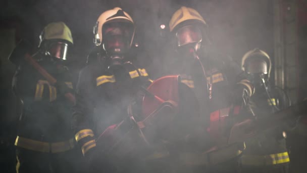一组身穿全套装备 氧气面罩和应急救援工具 圆形液压和气体锯子 斧头和雪橇锤的消防员 后面的烟雾和消防车 — 图库视频影像