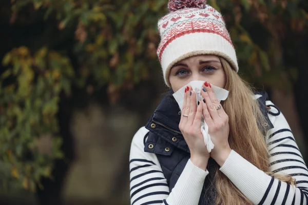 Pretty young woman blowing her nose with a tissue outdoor — Stock Photo, Image