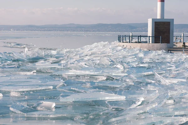 Beschaffenheit der Eisfläche, rissiges Eis, das auf blauem Wasser schwimmt, saisonale Winterlandschaft.Eisbedeckter Pier am Balaton. — Stockfoto