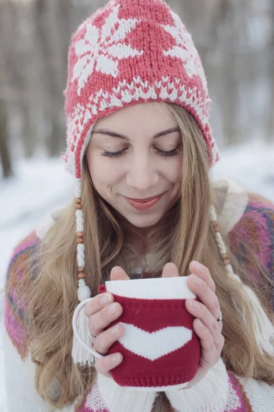 Mujer de invierno sosteniendo una taza para calentarse. Linda mujer joven bebiendo té o café al aire libre —  Fotos de Stock