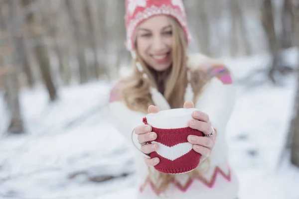 Közeli kép a nő keze gazdaság vicces csésze. A hangsúly a háttérben a téli erdő. — Stock Fotó