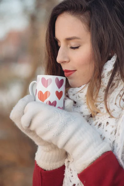 美しいの若い笑顔白人女性の冬のジャケット、スカーフ、コーヒーや紅茶のカップを保持している, アウトドア公園や冬の日の森でのクローズ アップの肖像画。冬気分 — ストック写真