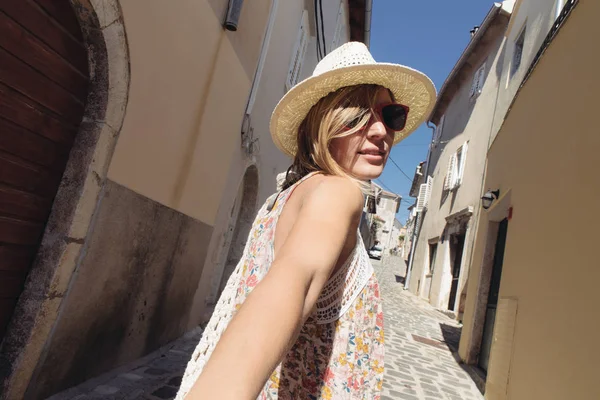 Vrouw die haar man te volgen haar in de vakantie of huwelijksreis. Vrouw in modieuze zomerjurk met hoed man met de hand te houden en te gaan sightseeën. — Stockfoto