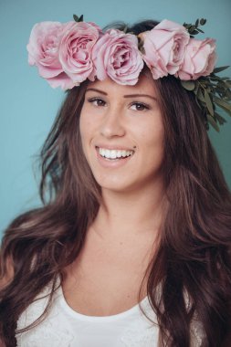 Çiçek çelenk, pastel bahar renkleri ile gülümseyen genç kadın. Pembe Gül çelenk başında. Uzun saçlı esmer kadın.
