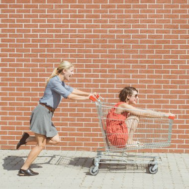 Arkadaşlar bir alışveriş merkezinde alışveriş sepeti ile eğleniyor