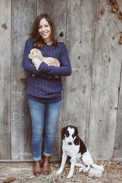 Mujer adulta joven con cabra bebé y perro joven en la granja — Foto de Stock