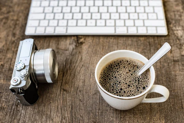 Office table with computer keyboard, cup of coffee and vintage camera. Retro camera on rustic wooden desk. Copy space. — Stock Photo, Image