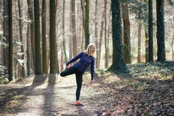 Actieve jonge vrouw die zich uitstrekt buiten in het bos — Stockfoto