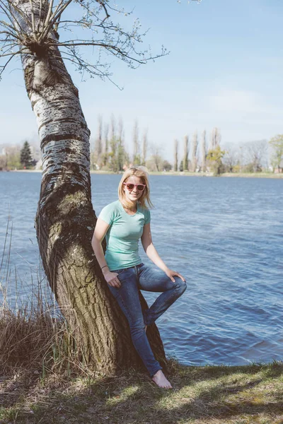 Mladá žena odpočívá v letním parku. Jeden strom a jezero na pozadí. — Stock fotografie