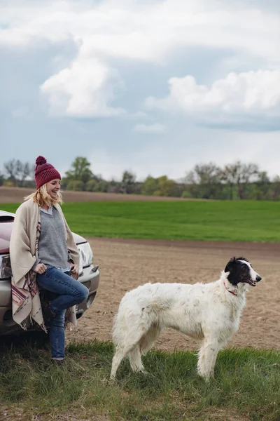 オフロードで立っている農夫女性彼女のロシアのグレイハウンド犬と車. — ストック写真