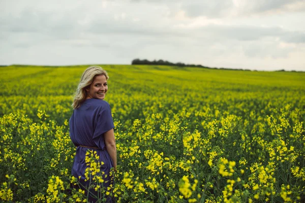 Mujer joven de pie al aire libre en el campo de flores de colza y sonriendo —  Fotos de Stock