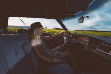 kadın araba iç etrafında dönen ve gülümseyen, gün batımı ışınlarına karşı kadın sürücü tekerleği tutar