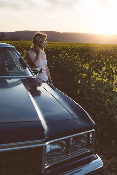 Giovane donna in posa da auto d'epoca al tramonto — Foto Stock