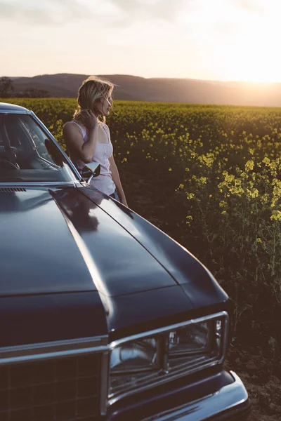 Mujer joven posando en coche vintage al atardecer —  Fotos de Stock