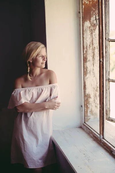 Roztomilý blond žena doma s otevřenýma očima, při pohledu z okna — Stock fotografie