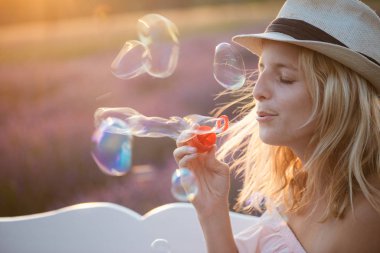 Gün batımında sabun köpüğü üfleme şirin sarışın kadın. 