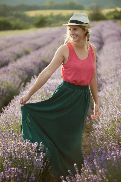 Jovem mulher em um vestido agradável e chapéu de palha correndo em um campo de lavanda — Fotografia de Stock