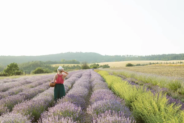 Jovem mulher em um vestido agradável e chapéu de palha correndo em um campo de lavanda — Fotografia de Stock