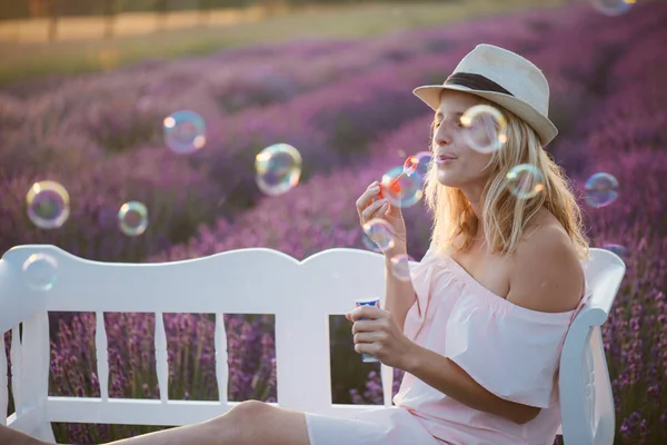 Schöne Frau, die Seifenblasen auf einer Bank pustet. herrliches Lavendelfeld im Hintergrund. — Stockfoto