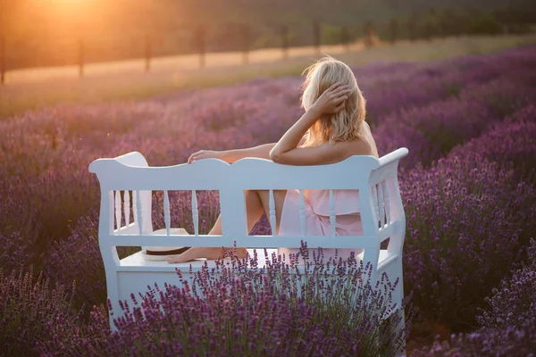 Donna che guarda il tramonto sul campo di lavanda. Panchina vintage nel mezzo di un campo di fiori . — Foto Stock