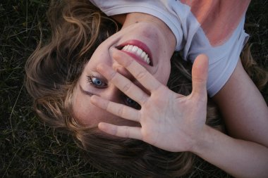 çim üzerinde yalan ve yüz el ile kapsayan mutlu genç kadın yakın çekim, 