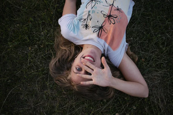 Счастливая женщина лежит на траве и закрывает лицо ладонью. — стоковое фото