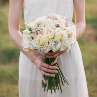 yeşil bir bahçede duran ve bir düğün buket çiçek ve yeşillik tutan bir elbise içinde gelin. Düğün gününde onunla renkli buket tutan kadın eller